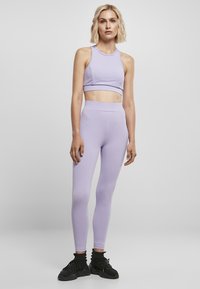 Lys lavendel treningssett med en kort tanktopp og høyt liv leggings, laget av glatt, elastisk materiale, paret med svarte joggesko.