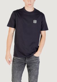 T-shirt a maniche corte blu navy realizzato in cotone morbido, con una piccola patch del logo sul lato sinistro del petto. Texture liscia con scollo rotondo.