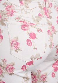 Vaqueros blancos con estampado floral de rosas en tonos rosa y beige, con bolsillos traseros y costuras en contraste. Fabricados en una suave mezcla de algodón.