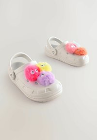 Biele gumové nazúvaky s tromi farebnými, chlpatejšími pompónmi v ružovej, žltej a purpurovej farbe. Majú bočné ventilačné otvory a zadný remienok.