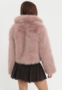 Faux fur jakke i blød pink, med høj krave og lange ærmer. Bæres over en sort plisseret denimnederdel med frynsede kanter.