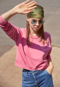Svetlo roza majica s crew vratom in rebrastimi manšetami, kombinirana z modrimi hlačami z visokim pasom. Dodatki vključujejo zeleno vzorčasto rutko in sončna očala.