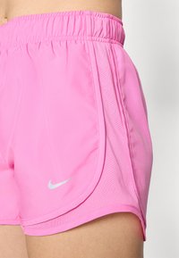 Shorts sportivi da donna Nike in un vivace rosa, caratterizzati da una vita elastica e pannelli laterali in rete traspirante, con un accento in argento del logo.