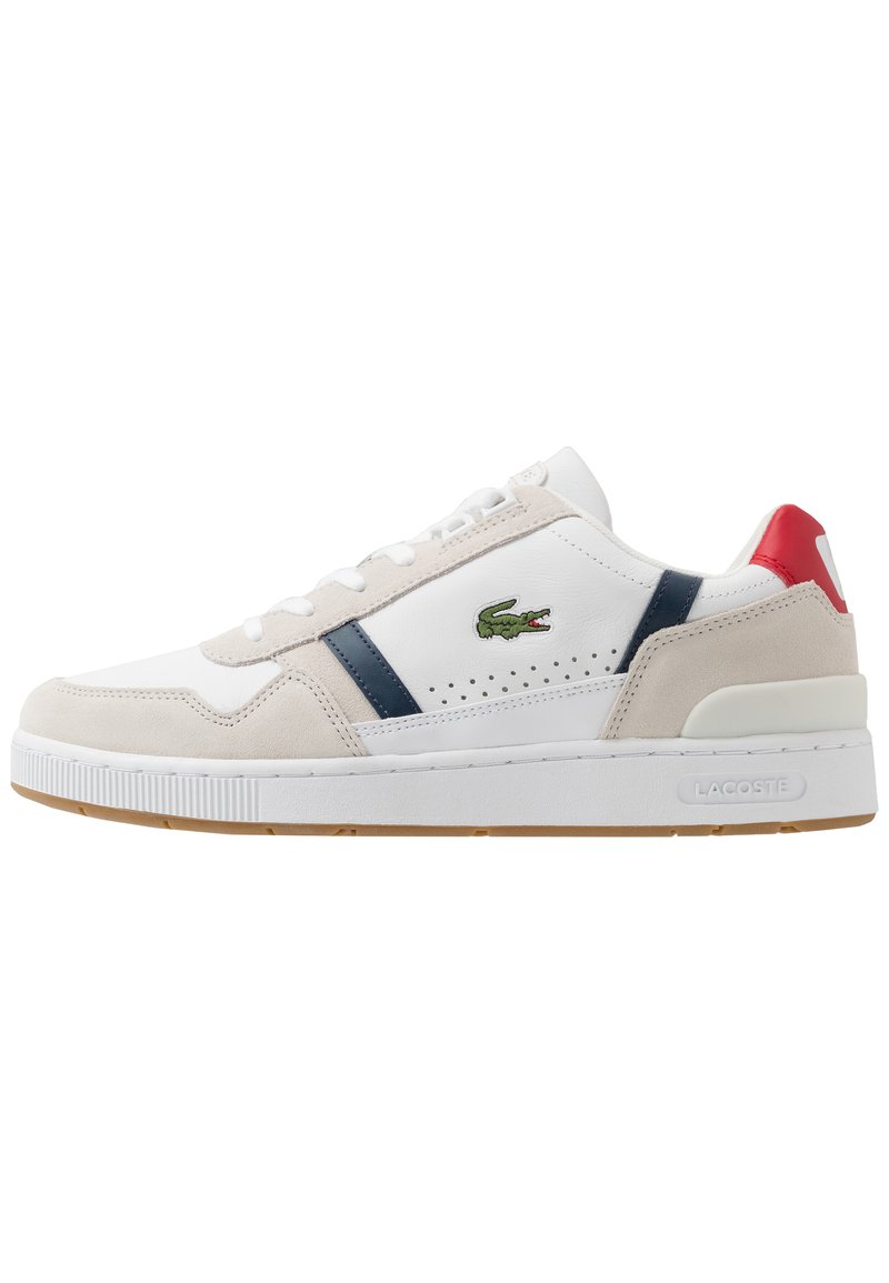 Vit och beige sneaker med marinblå och röda accenter. Funktioner i mocka och läder, en perforerad design och en gummisula. Lacoste-logotypen visas.