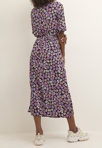 Robe fleurie avec un fond noir orné de petites fleurs violettes, roses et blanches. Longueur mi-longue, tissu léger avec taille froncée et fentes latérales.