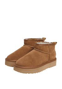 Botas de tobillo de ante marrón con un suave forro interior, caña corta y suela de goma texturizada. El diseño incluye detalles de costura.