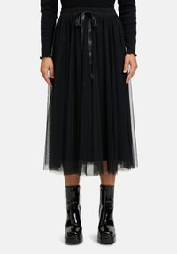 Gonna di tulle nera con una fascia larga in vita, dotata di un laccio in satin. Abbinata a stivali con plateau neri lucidi per un contrasto.
