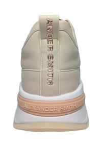 Sneaker color crema con una parte superiore testurizzata, dotata di un tallone imbottito e di accenti con il nome del marchio in rilievo di un elegante rosa metallizzato. Base della suola bianca.