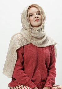 Sweter dziany w głębokim czerwonym kolorze, w zestawieniu z jasnobeżowym, teksturowanym szalikiem, który swobodnie opada na ramiona i głowę. Miękka, przytulna tkanina.