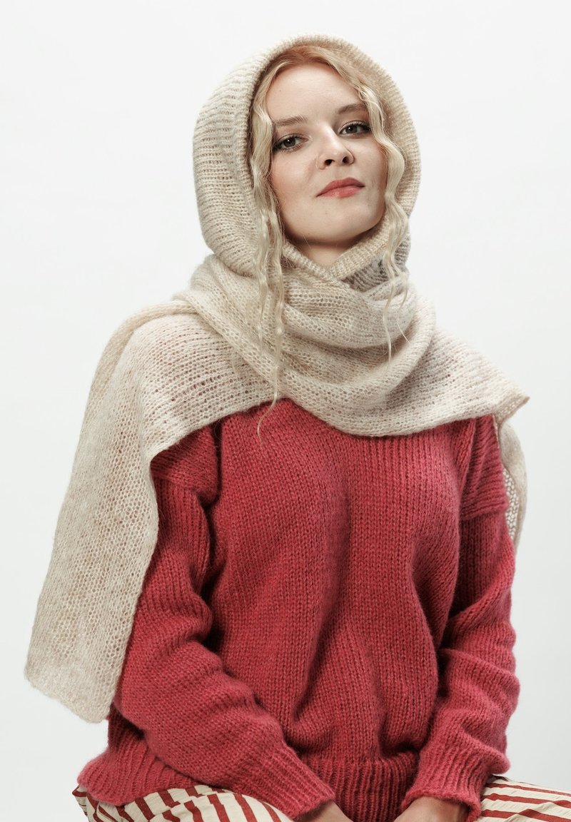 Sweter dziany w głębokim czerwonym kolorze, w zestawieniu z jasnobeżowym, teksturowanym szalikiem, który swobodnie opada na ramiona i głowę. Miękka, przytulna tkanina.