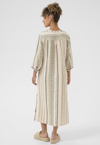 Robe en coton rayée, longue, dans des verts pastels, roses et des teintes neutres. Dispose d'un empiècement au dos et de manches 3/4 avec des détails texturés.
