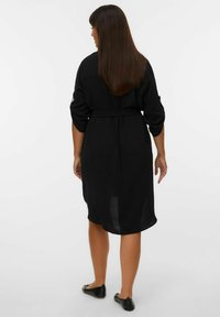 Zwarte midi-jurk met een losse pasvorm, een ceintuur in de taille, driekwart mouwen en een lichte textuur. Eenvoudig, klassiek ontwerp zonder patronen.