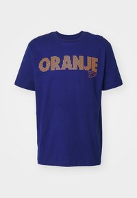 T-shirt en coton bleu marine avec "ORANJE" en strass orange, col rond, manches courtes, et un petit logo Nike en bas à gauche.