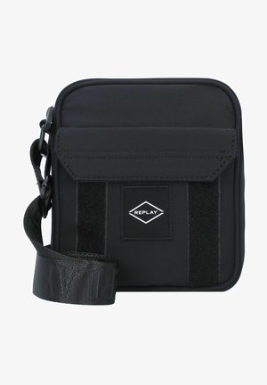 Black fabric crossbody bag with a flap closure, Velcro accent, adjustable strap, and a small logo patch in a diamond shape.