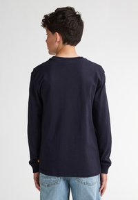 Camiseta de algodón de manga larga en color marino con cuello redondo, puños acanalados y sin gráficos, combinada con jeans de mezclilla de color azul claro.