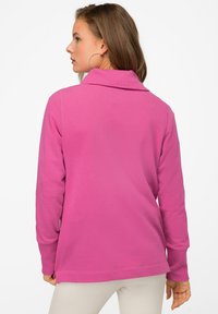 Pullover a maniche lunghe in tessuto fucsia vivace con colletto ripiegato, vestibilità rilassata e polsini a costine. Texture liscia e design minimalista.