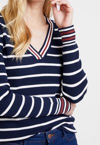 Marineblauer gestreifter Pullover mit weißen Streifen und rotem Akzent am Halsausschnitt und an den Ärmelbündchen; gerippte Textur und V-Ausschnitt-Design.