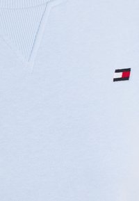 Maglione a maglia di un blu chiaro con scollatura a V. Presenta un piccolo logo ricamato in rosso, bianco e nero sul lato sinistro del petto. Texture morbida.