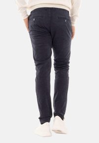 Chinos navy con una texture liscia, vestibilità aderente, due tasche posteriori e un dettaglio con bottone. Abbinati a sneaker bianche, design minimal.