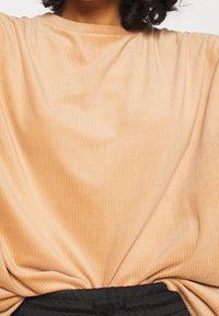 Haut texturé couleur pêche avec un design côtelé et une coupe décontractée, associé à une ceinture noire. Tissu lisse, encolure modeste.