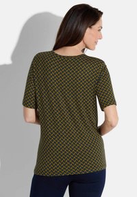 Blouse à motif en vert foncé avec un design géométrique jaune. Manches courtes, encolure ronde, tissu doux et coupe décontractée.