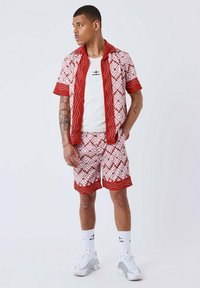 Camisa corta de manga corta en rojo y blanco con patrones geométricos, combinada con pantalones cortos a juego. Top de tirantes blanco debajo, zapatillas blancas y calcetines.