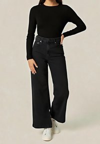 Jean noir à jambes larges avec une taille haute, un design à cinq poches et des coutures frontales discrètes, assorti à un haut noir ajusté à manches longues et des baskets blanches.