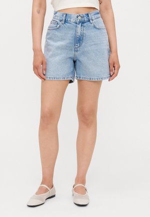 Lysblå denim shorts med høj talje, lige pasform, frynset kant og frontlommer. Parret med beige lukkede sko.