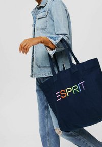 Sac fourre-tout bleu marine avec deux poignées, arborant le logo "ESPRIT" brodé multicolore. Matière en toile de coton, forme rectangulaire et sans fermetures.