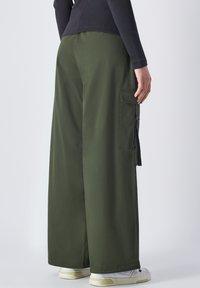 Cargo broek met wijde pijpen in olijfgroen katoen, met zijzakken en een losse pasvorm. De broek heeft een zachte textuur en een duurzame uitstraling.