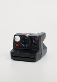 Polaroid instant camera with a black plastic body, a circular lens, red button, and rainbow stripe. Features a slot for photo output.