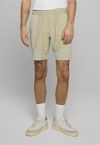 Los pantalones cortos deportivos beige tienen una textura suave, una cintura elástica y bolsillos laterales. Combinados con calcetines blancos y zapatillas de color claro.