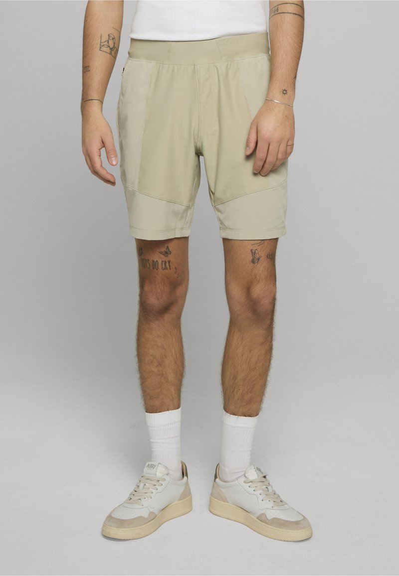 Los pantalones cortos deportivos beige tienen una textura suave, una cintura elástica y bolsillos laterales. Combinados con calcetines blancos y zapatillas de color claro.