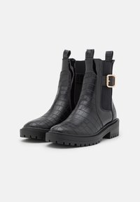 Botas negras hasta el tobillo con textura de piel de cocodrilo, lados elásticos, un detalle de hebilla dorada y una suela gruesa de goma con dibujo.