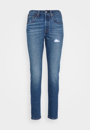 Jeans en denim bleu avec une coupe slim, taille mi-haute, légère déchirure et coutures contrastées. Comprend cinq poches et une fermeture à bouton traditionnelle.
