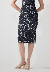 Abito midi nero con un motivo astratto bianco, caratterizzato da un design aderente e una texture arricciata. Abbinato a sandali con tacco a strisce beige chiaro.