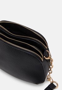 Sorte lædertaske med en struktureret overflade, tre lynlåslommer og hardware i guld-tone med en kædeaccent.