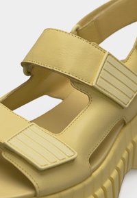 Κοντινό πλάνο ενός μπεζ σανδαλιού με ρυθμιζόμενους ιμάντες βέλκρο και χοντρή, ραβδωτή σόλα.