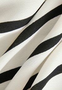 Tkanina w czarno-białe paski o teksturowanej powierzchni, z diagonalnymi liniami i miękkim układem.