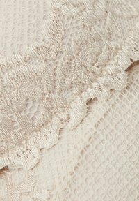 Béžová krajková tkanina s texturovaným vzorem a volánkovými okraji. Povrch je hladký s jemnými detaily, ideální pro oděvy nebo doplňky.