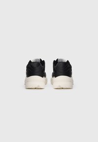 Pair of black and white sneakers viewed from the back on a plain light gray background, showing thick white soles and padded heels.