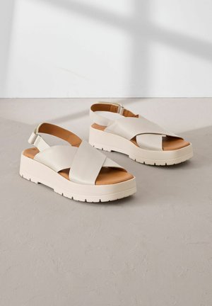 Sandales à plateforme beiges en cuir lisse avec des brides croisées, une sangle pour la cheville et une semelle en caoutchouc texturé pour l'adhérence.
