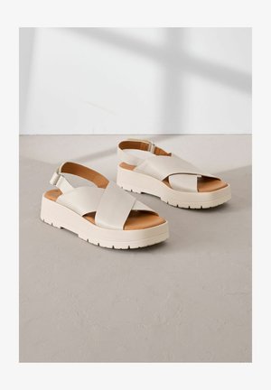 Bežové platformové sandály vyrobené z hladké kůže s křížovými popruhy, s páskem kolem kotníku a texturovanou gumovou podrážkou pro lepší přilnavost.