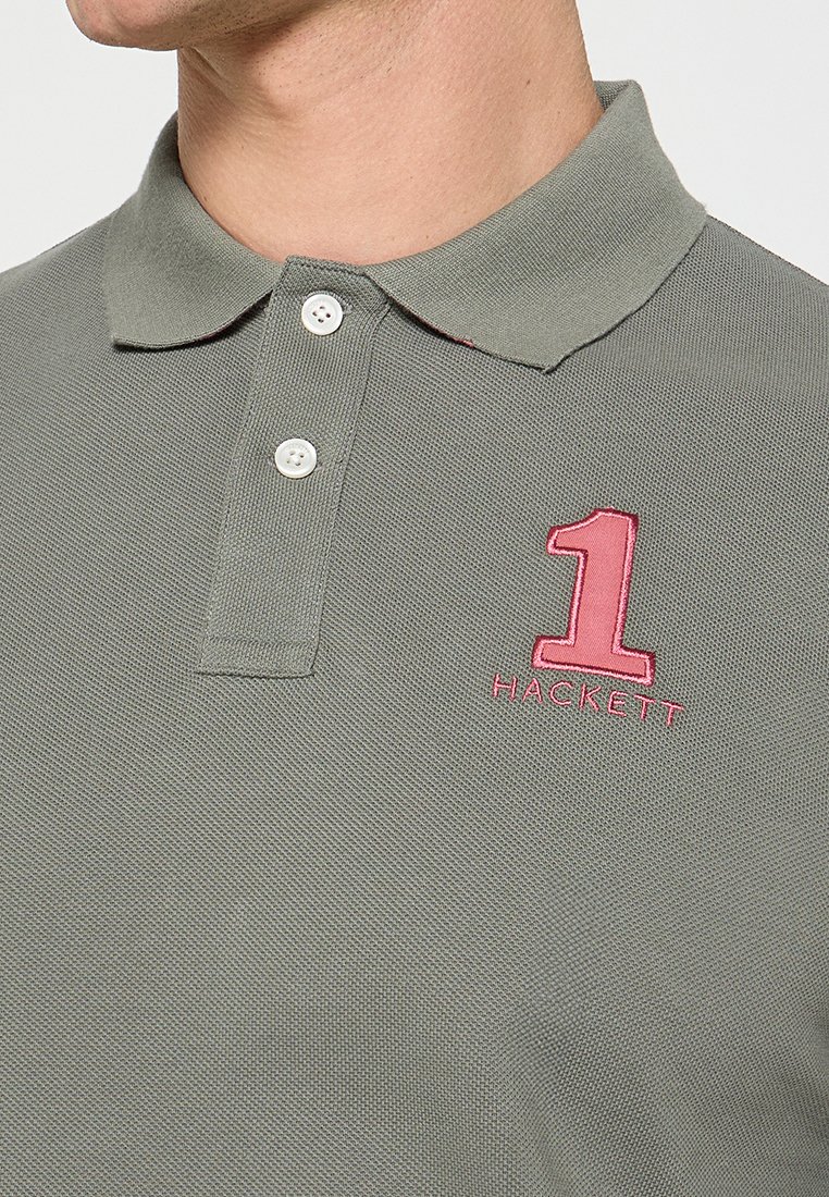 Gray polo shirt made of textured fabric with a two-button placket, featuring a large pink embroidered '1' and the word 'HACKETT.'