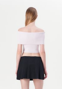 Lichtroze, geribbelde off-shoulder crop top gecombineerd met een zwarte geplooide minirok, met een aansluitend ontwerp en een gladde textuur.