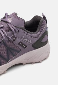 Zapatilla deportiva morada con una parte superior de malla transpirable, acentos negros, superposiciones texturizadas y una suela de goma resistente. Marca en el lateral.