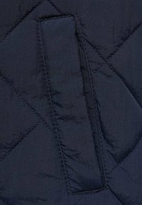 Námořnická prošívaná látka má diamantové vzory a boční kapsu, vyrobenou z hladkého, lesklého materiálu, který zdůrazňuje její lehký design.