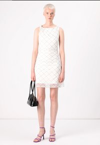 Vestido blanco sin mangas con un patrón geométrico texturizado, combinado con tacones morados y un bolso negro, con una silueta ajustada.