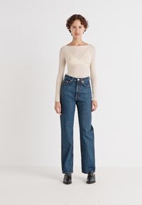 Beež pika-õnguga bodi pikkade varrukatega, millele on sobitatud kõrge vöökohaga sinised denim Sirge lõikega teksad ja mustad kingad.
