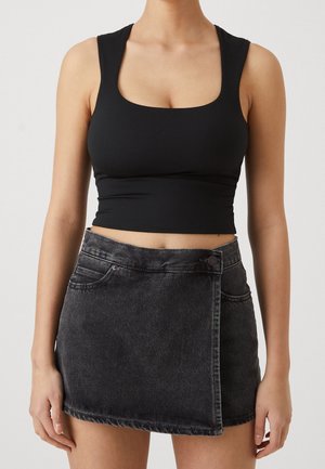 Vrouw draagt een zwarte cropped tanktop en een hoog getailleerde donkergrijze denim minirok met knopen aan de voorkant en overslagdetail.